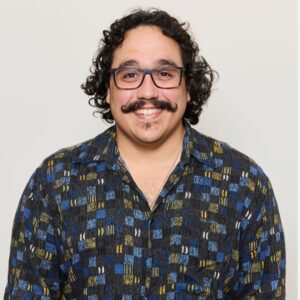 A head and shoulders image of a smiling man with dark hair, glasses and moustache